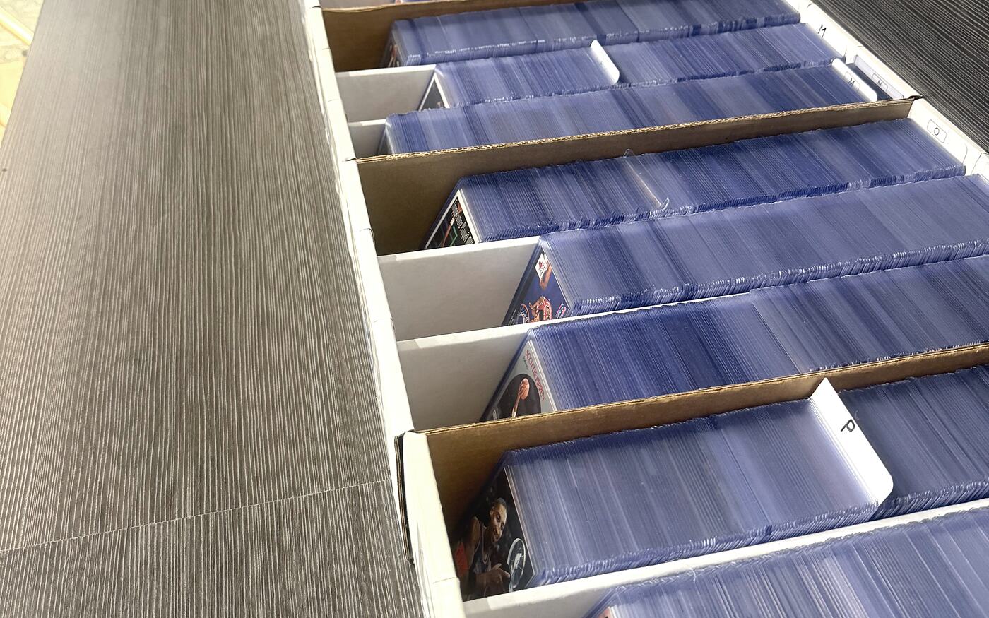 Rows of white card boxes on the browse table, packed with penny-sleeved singles behind handwritten dividers.