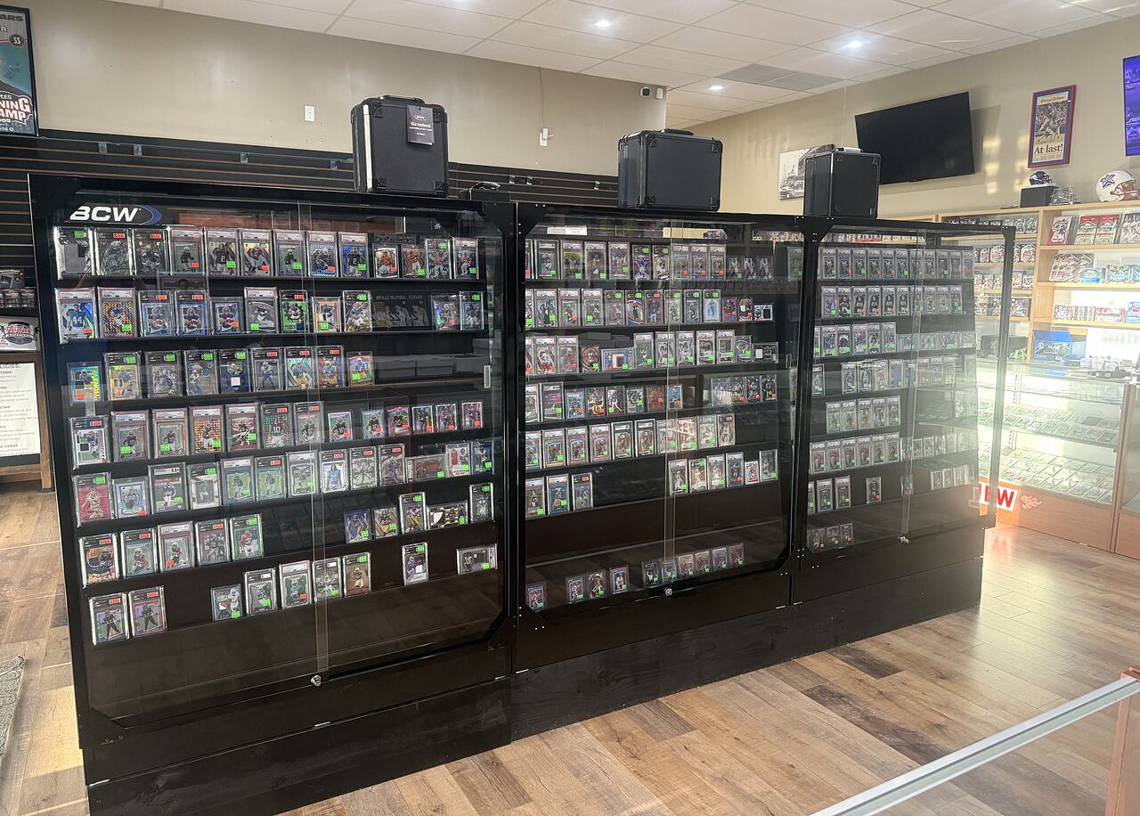 A wall of locked glass cases at the Kearney shop holding several hundred graded slabs, front-facing in rows on black shelving.